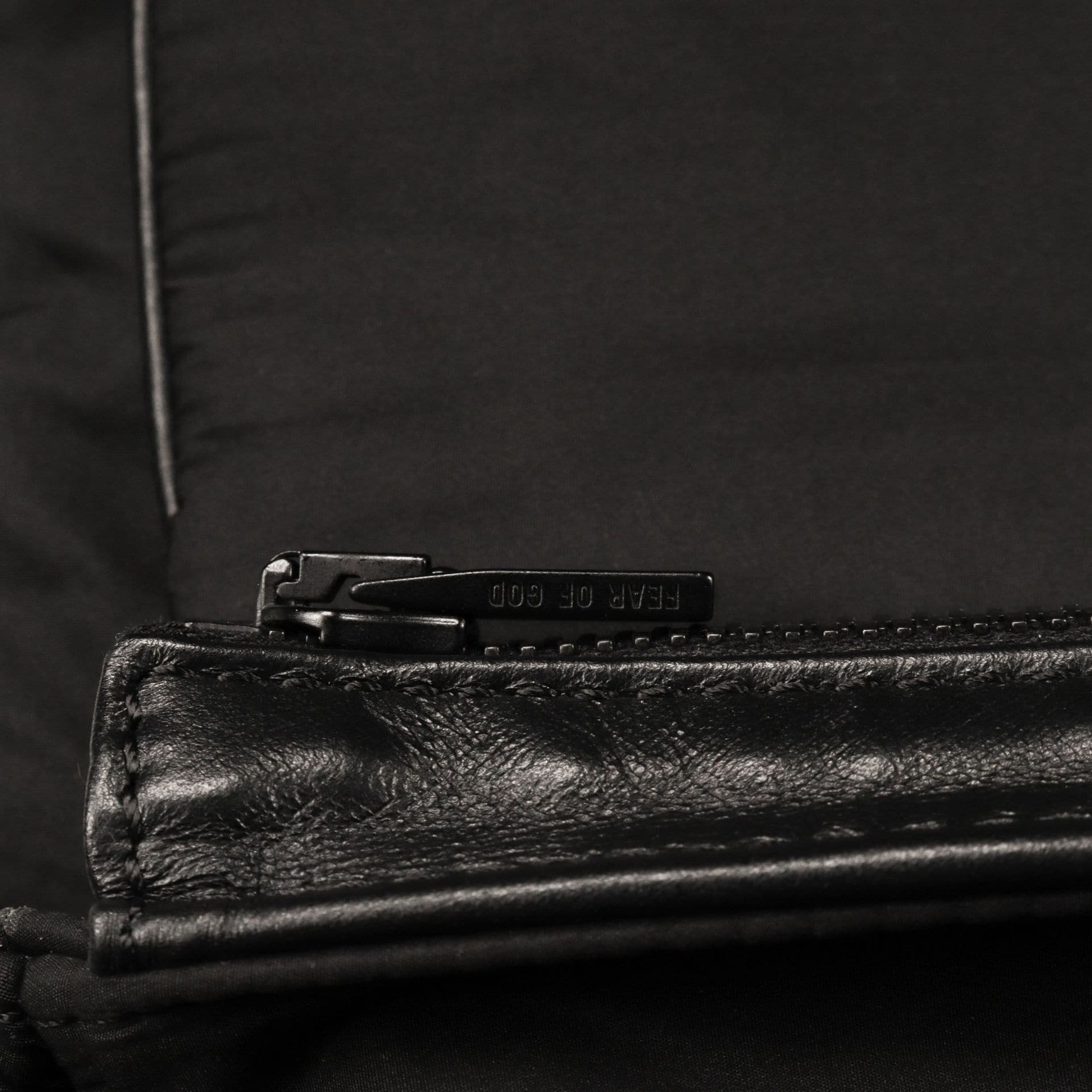 Earp of GCD zipper on black fabric, close-up detail of leather-like material with stitching.