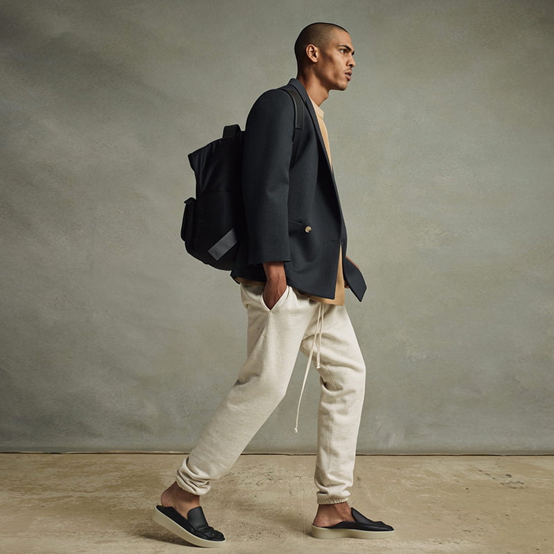 Black and beige casual streetwear look with a backpack, joggers, and slides, perfect for K-pop merch fans.