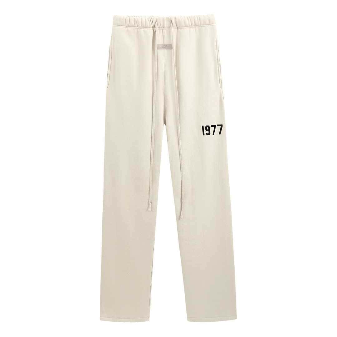 Cream-colored sweatpants with "1977" printed on the thigh, casual streetwear style, drawstring waistband and relaxed fit, minimalistic and trendy.